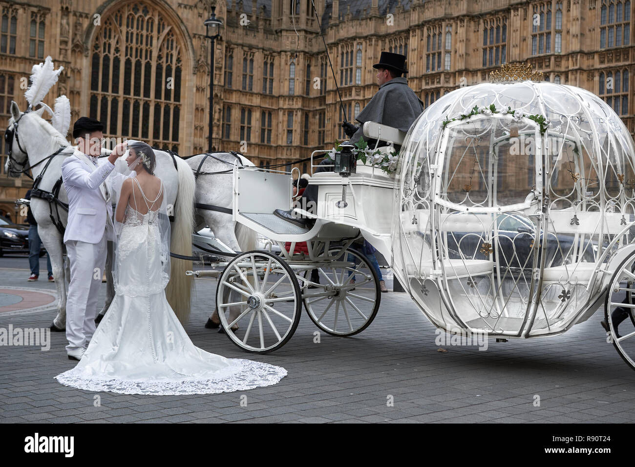 Chinesisches Ehepaar in Weiß gekleidet posieren für märchenhafte Hochzeit Fotos, mit weißen Schlitten mit zwei weißen Pferden, außerhalb des Parlaments, London gezeichnet. Stockfoto