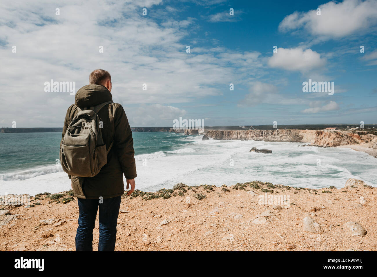 Ansicht von hinten von einem Mann Tourist oder ein Kerl mit einem Rucksack bewundert die schöne Landschaft und das Meer in Einsamkeit und denkt oder Träume. Stockfoto