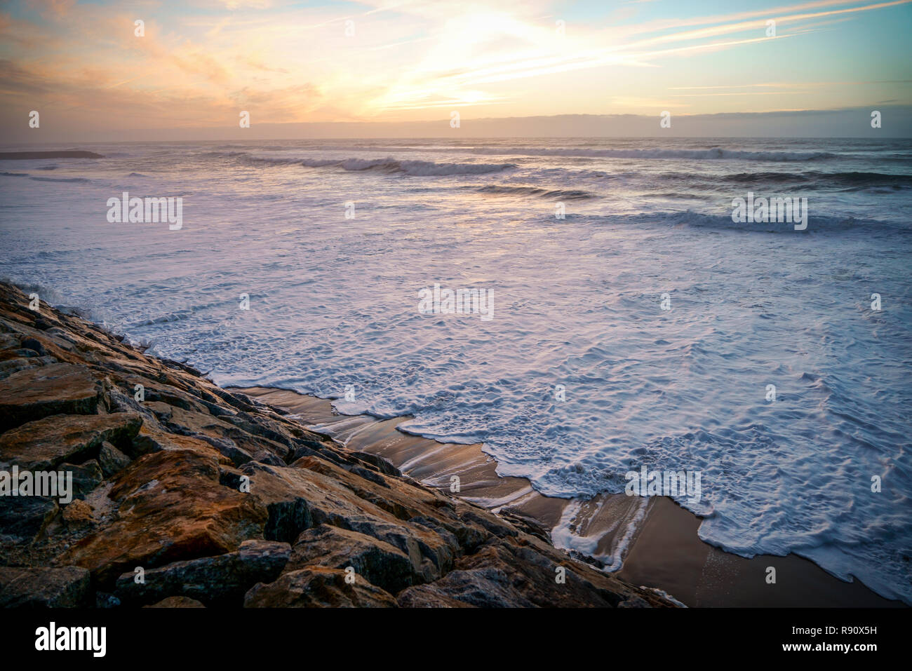 Ozean Wellen mit weißen Schaum sanft in die bemoosten Felsen gegen einen schönen Herbst Sonnenuntergang. Mit kopieren. Stockfoto