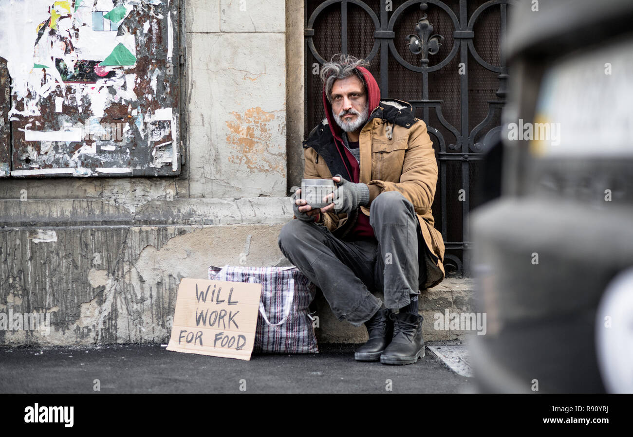 Eine obdachlose Bettler Mann sitzt vor der hölzernen Tor draußen in der Stadt bitten um Geld Spende. Stockfoto