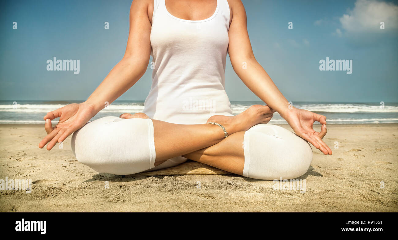 Frau tut Yoga Meditation im weißen Kostüm am Strand von Goa, Indien Stockfoto