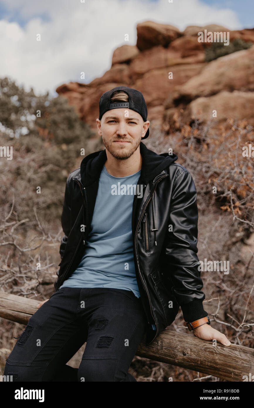 Porträt der Jungen gut aussehenden Casual Reisen schöner Mann außerhalb lächelnd in der Nähe von Ancient Desert Red Rocks in Jacke Stockfoto