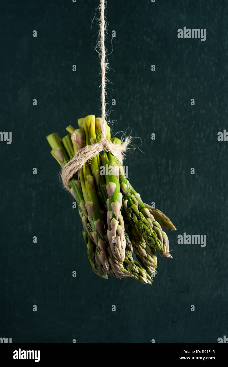 Nahaufnahme von einem Bündel Spargel an einem Hanf string, gegen einen dunkelgrünen Hintergrund Stockfoto