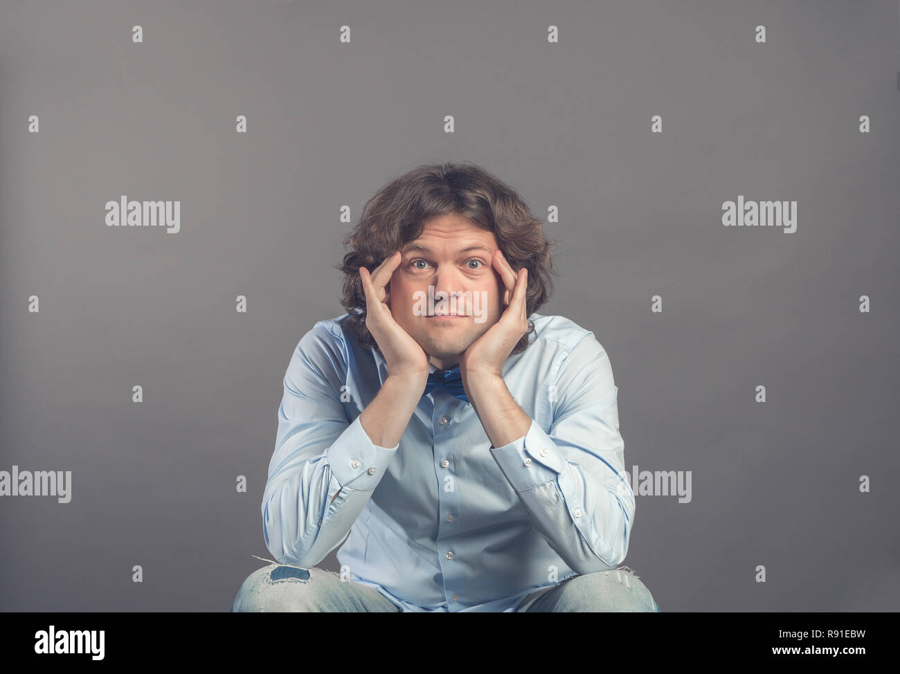 Portrait des jungen Mannes im Studio, ruht das Kinn auf die Hände, beim Sitzen und stützte die Ellbogen auf den Knien. Die Augen weit geöffnet, in die Kamera schauen und lächeln. Weari Stockfoto