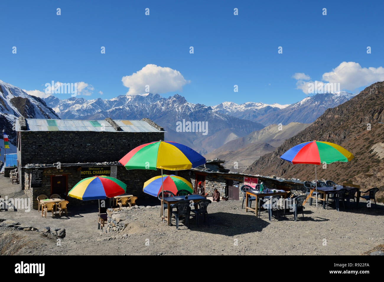 Ein teehaus unter Thorong La Pass, auf dem Annapurna Circuit, Nepal. Mit bunten Sonnenschirmen außerhalb mit der gezackten Gipfeln des Himalaya hinter Stockfoto