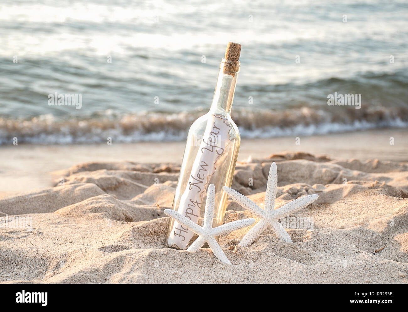 Frohes Neues Jahr Nachricht in einer Flasche mit Paar weiße Seesterne in Sand und Meer Wasser Hintergrund Stockfoto