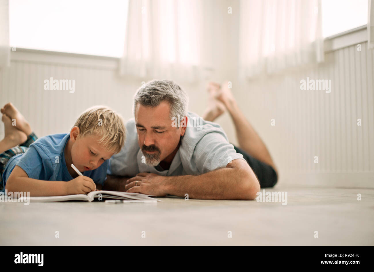 Reifen erwachsenen Mann auf dem Boden liegend, sein Sohn, Hilfe bei den Hausaufgaben. Stockfoto