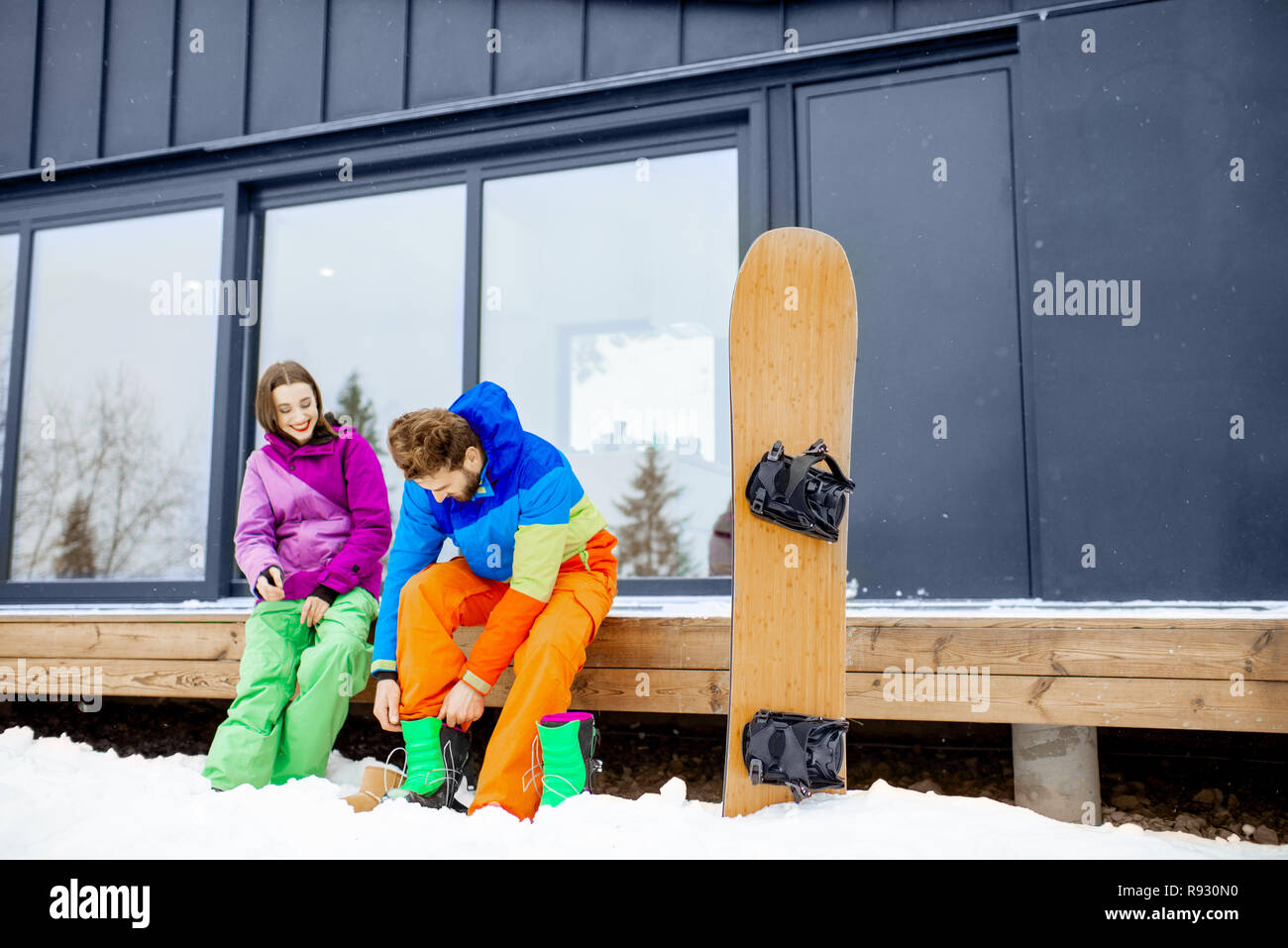 Junges Paar in skianzuege Vorbereitung für das Snowboarden sitzen auf der Terrasse des modernen Haus in den Bergen Stockfoto
