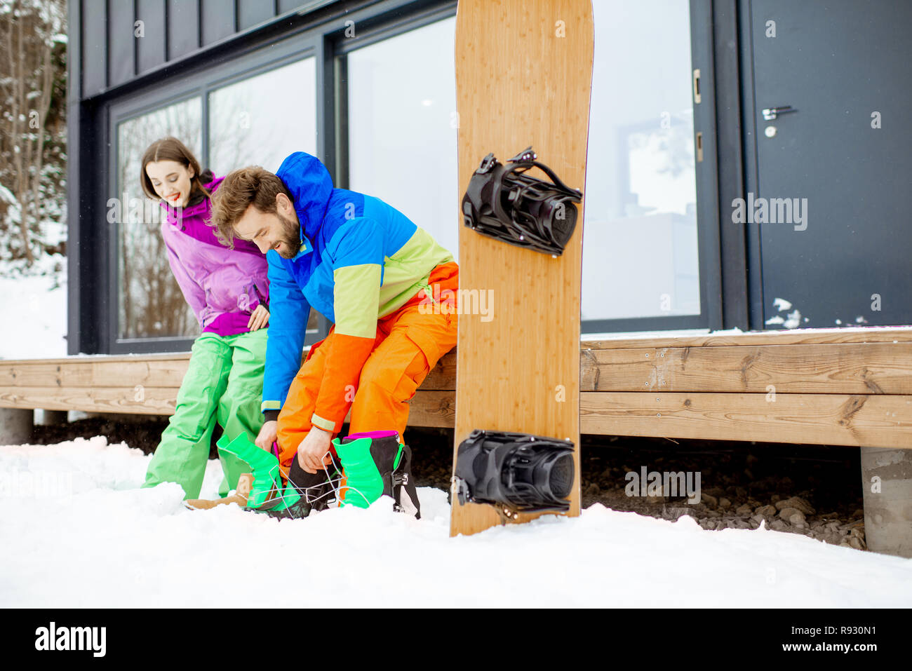 Junges Paar in skianzuege Vorbereitung für das Snowboarden sitzen auf der Terrasse des modernen Haus in den Bergen Stockfoto