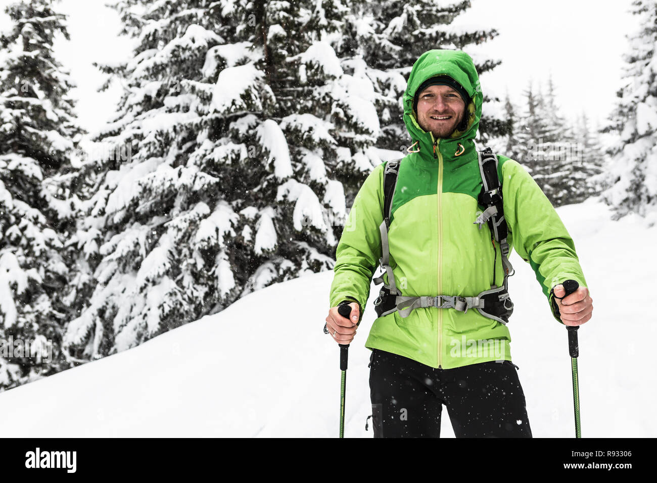 Lächelnd Mann zu Fuß auf Winter Trek in weiss verschneiten Wald, an der Kamera schaut. Menschen wandern im Winter Holz. Reisen und gesunden Lebensstil im Freien in Beau Stockfoto