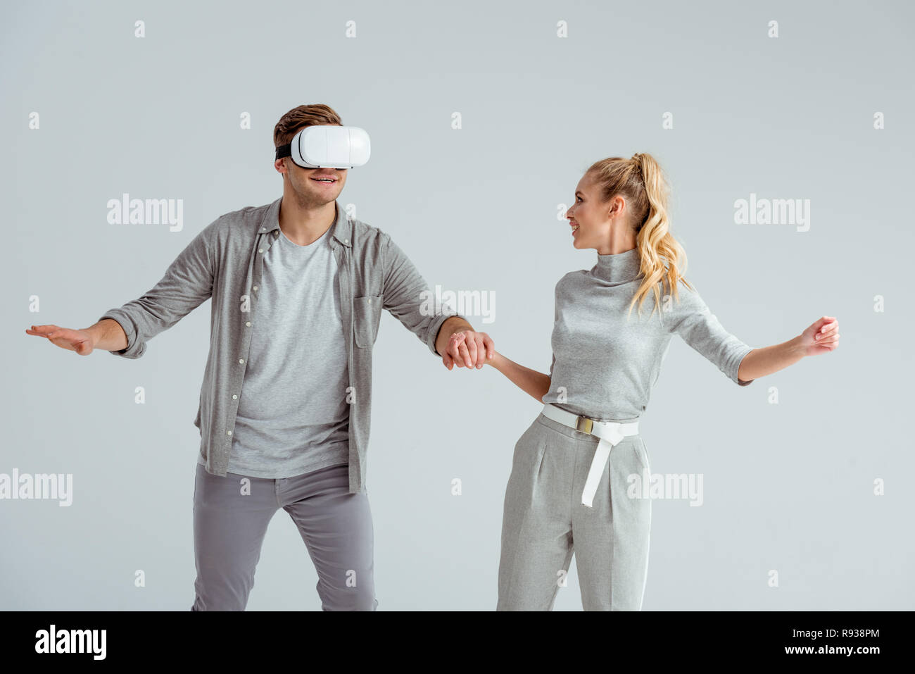 Paar in grauer Kleidung halten sich an den Händen, während Mann erleben virtuelle Realität isoliert auf Grau Stockfoto