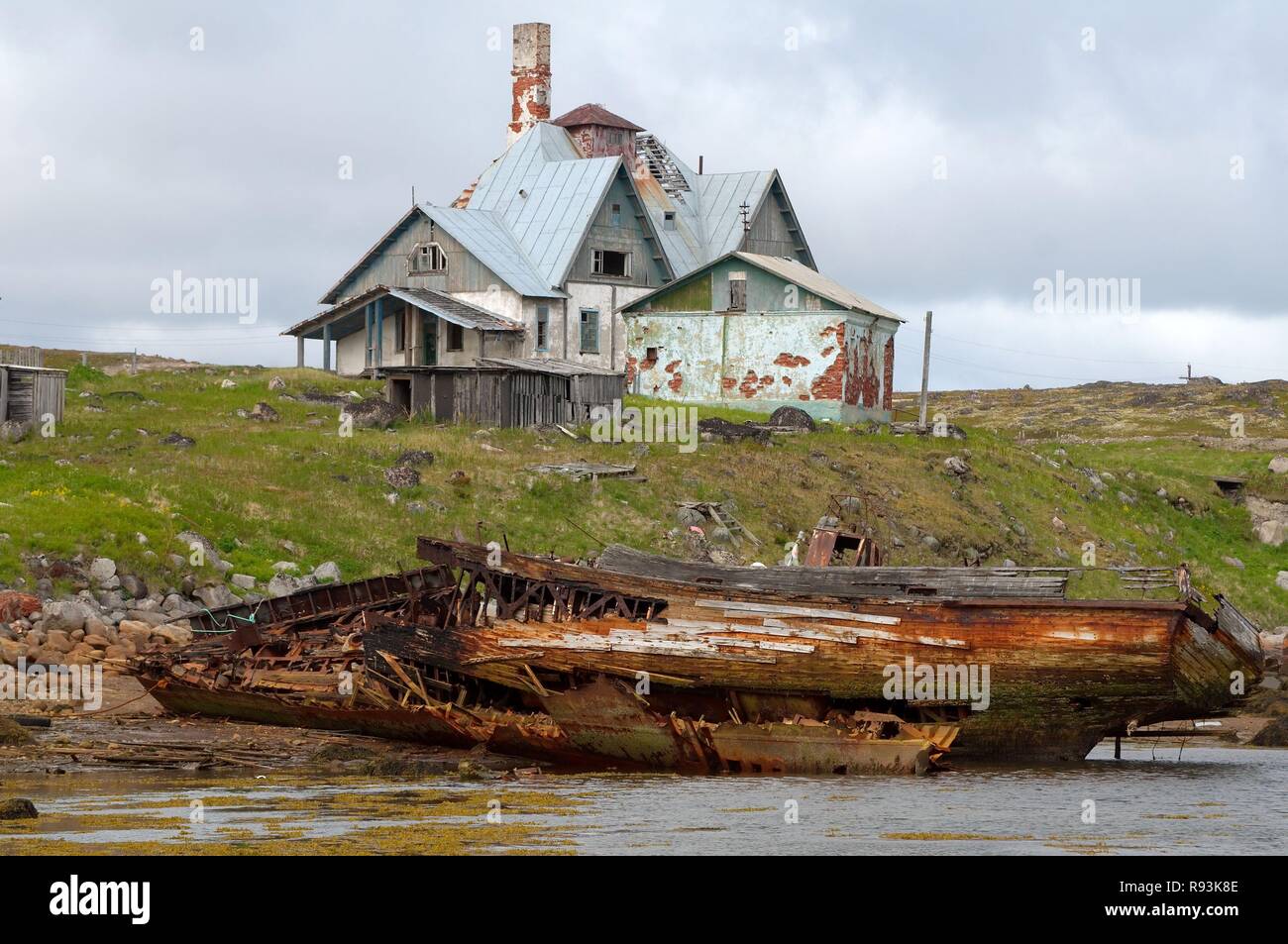 Heruntergekommenes kleines Fischerboot, MR, vor einem heruntergekommenen Haus in einer ländlichen Gegend in der Barentssee, Dalniye Zelentsy Stockfoto