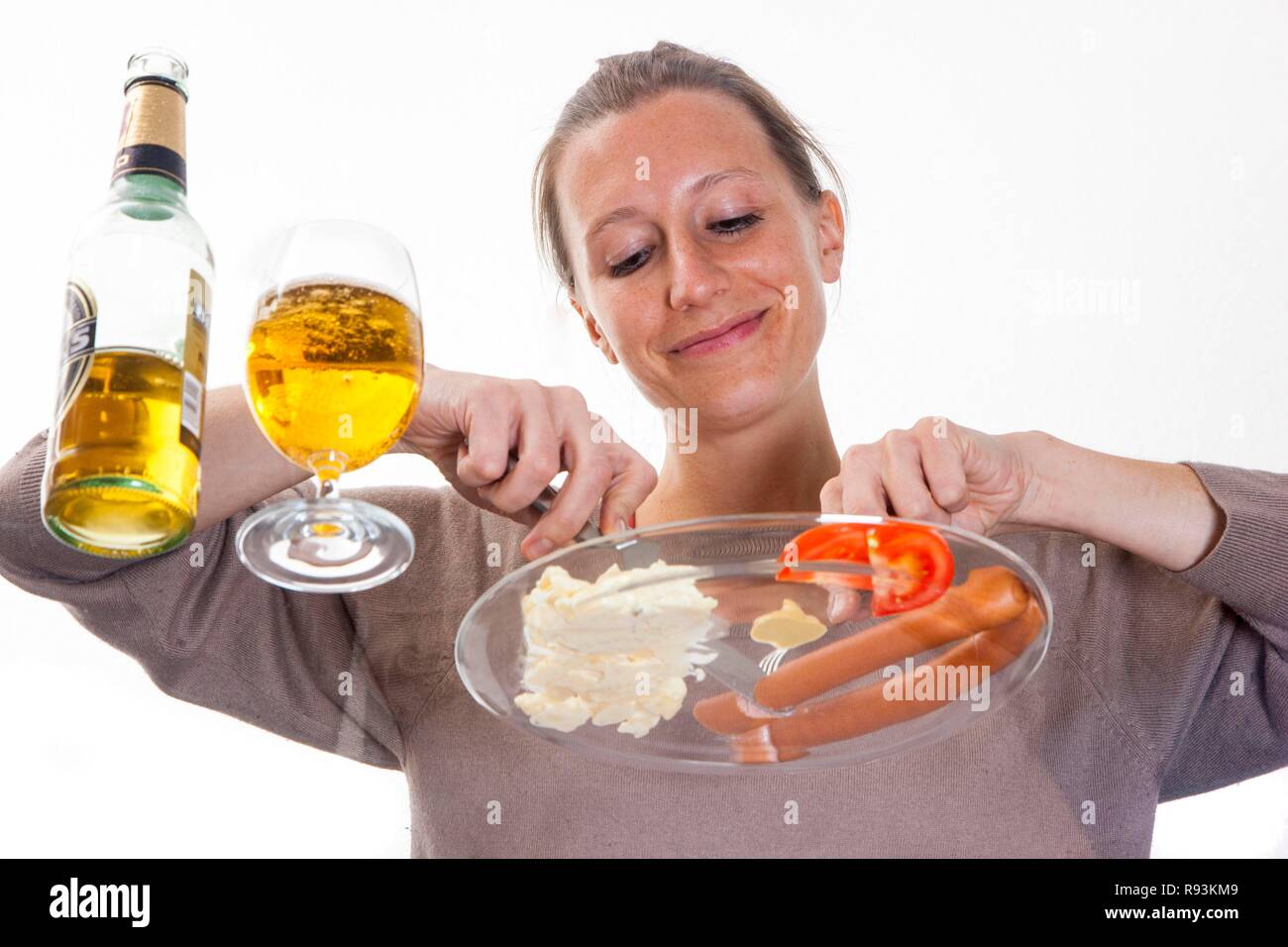 Junge Frau bei einem Glas Tisch essen Frankfurter Würstchen mit Kartoffelsalat, Senf und einem Pilsner Bier sitzen Stockfoto