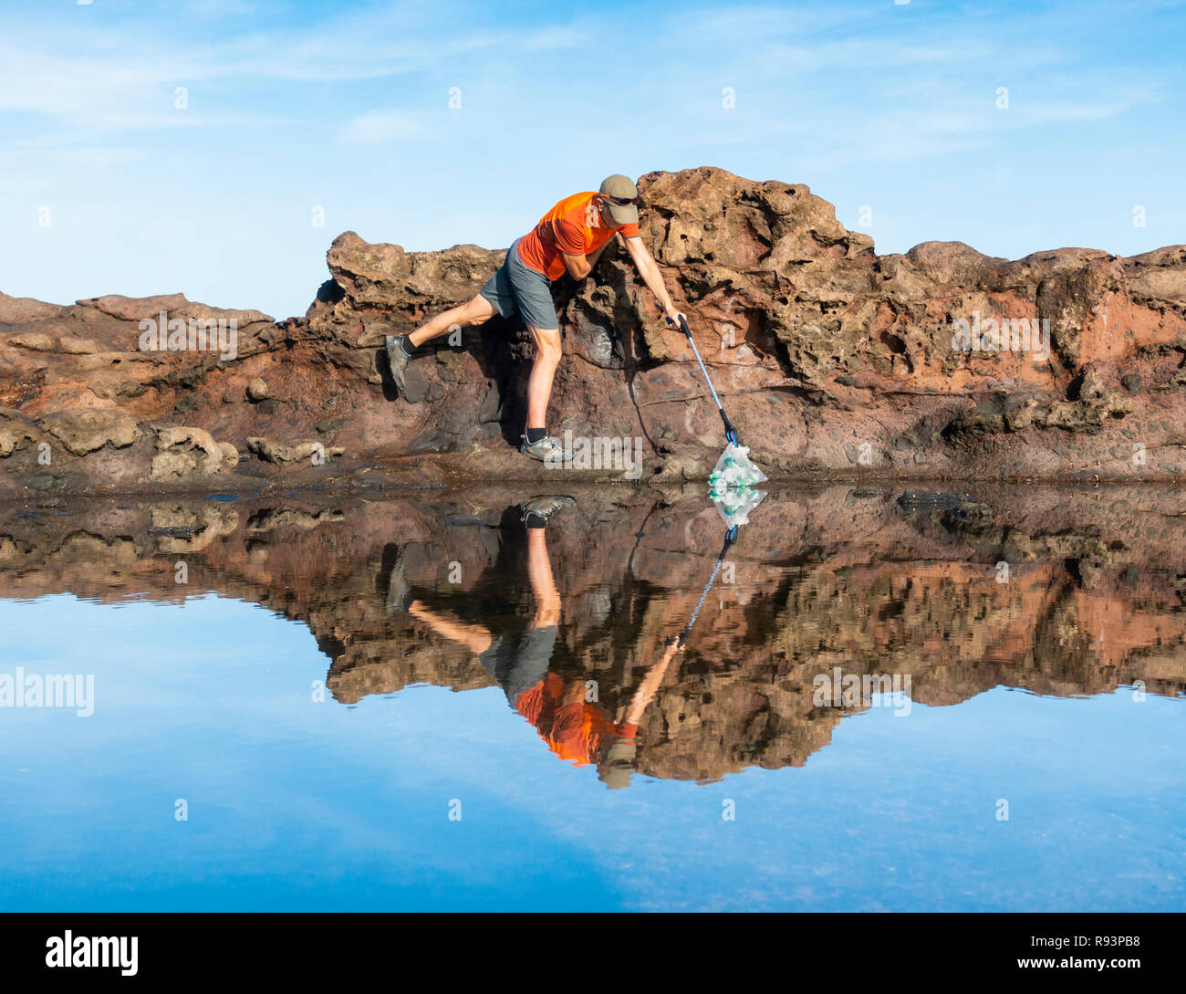 Ein Plogger/Jogger sammelt Plastikmüll am Strand während seines morgendlichen Lauf Stockfoto