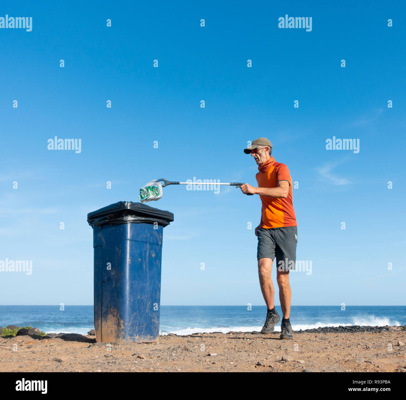 Ein Plogger/Jogger sammelt Plastikmüll am Strand während seines morgendlichen Lauf Stockfoto