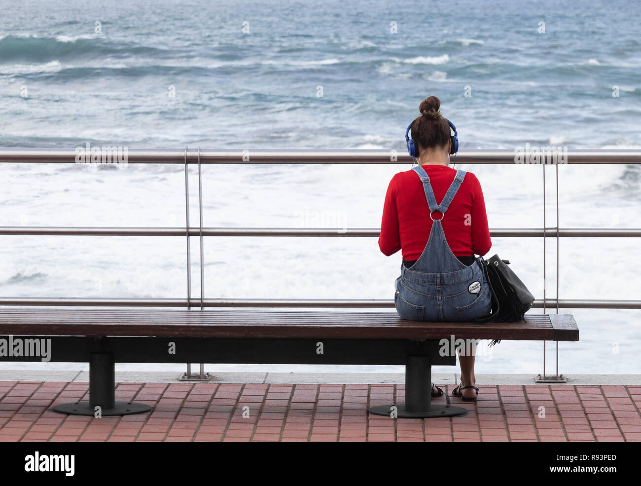 Ansicht der Rückseite des junge Frau mit Kopfhörern auf Sitz mit Blick auf das Meer. Stockfoto