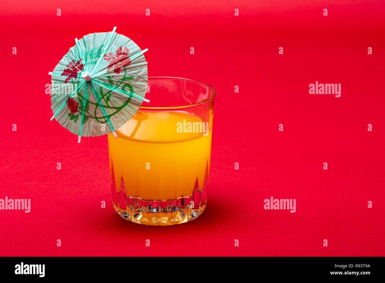Orange Drink auf rotem Hintergrund mit Regenschirm. Weiches Obst Drink mit einem Cocktail Regenschirm. Stockfoto
