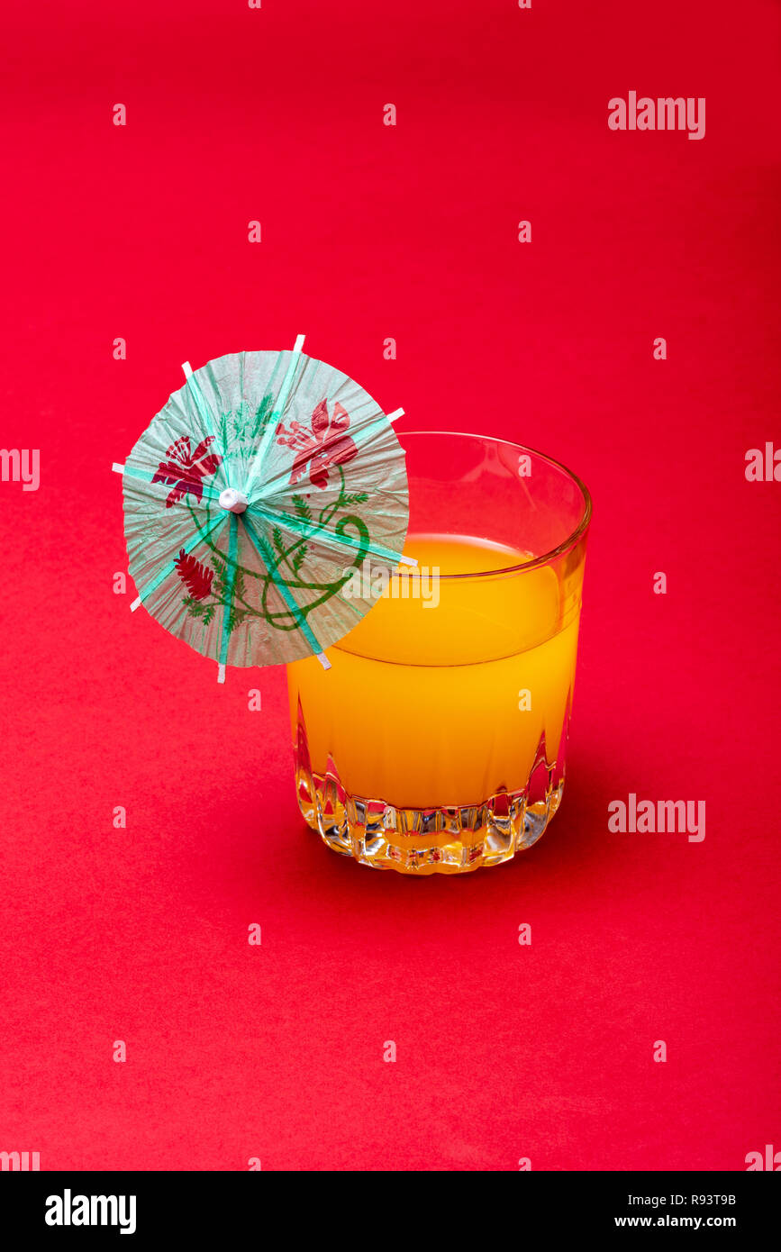 Orange Drink auf rotem Hintergrund mit Regenschirm. Weiches Obst Drink mit einem Cocktail Regenschirm. Stockfoto