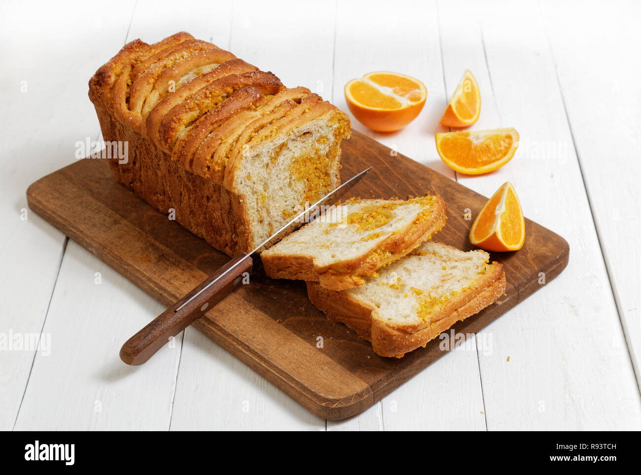 Hausgemachter Hefe Brot mit Orangenschale und Walnüsse auf weissem Holztisch. In der Nähe von einem Messer und Scheiben von frischen Orangen. Stockfoto