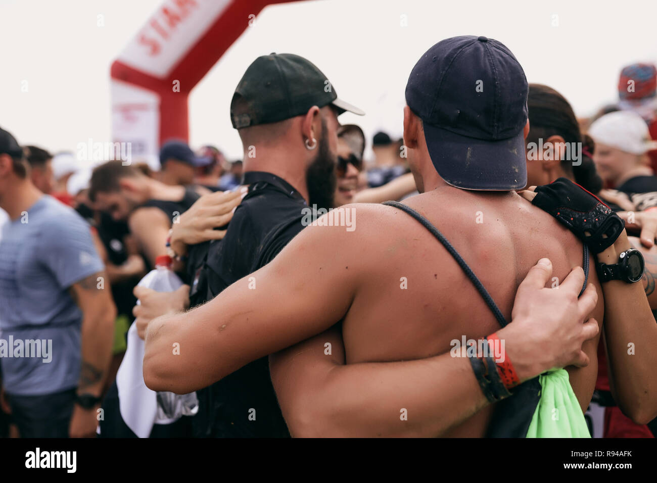 Sport im freien Wettbewerb. Eine Gruppe von Freunden zusammen umarmte. Starke Männer mit großen Muskeln, tragen Kappen auf dem Kopf, Zubehör auf dem Arm. Menge Stockfoto