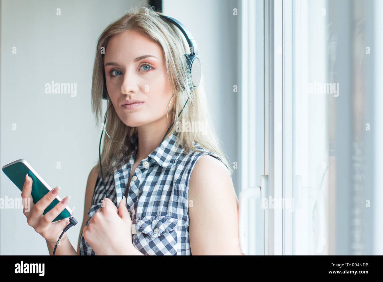 Schöne Mädchen in Plaid Shirt mit Kopfhörern Musik hören in Innenräumen, unscharfen Hintergrund, Kopf und Schultern, Jugend Musik Konzept Stockfoto