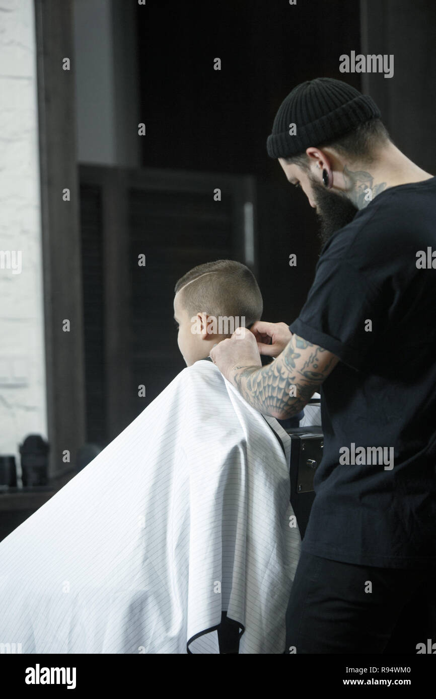 Kinder Friseur Schneiden kleiner Junge vor einem dunklen Hintergrund. Zufriedene cute Vorschüler Boy, die Haare schneiden lassen. Stockfoto