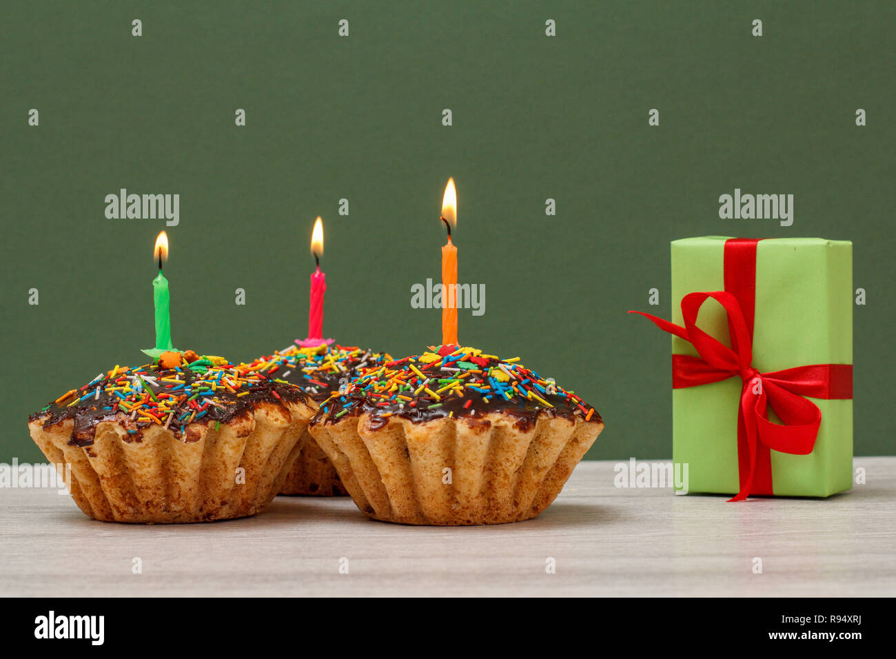 Geburtstag Drei leckere Cupcakes mit Schokoladenüberzug und Karamell, mit brennenden Kerzen und festlichen Geschenkverpackung auf grünem Hintergrund eingerichtet. Happy birthda Stockfoto