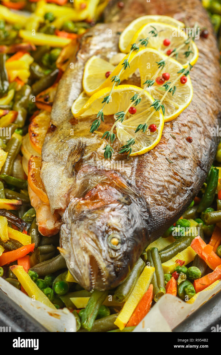 Gebackenen Fisch Forelle mit Gemüse (Kartoffeln, Karotten, Bohnen, grüne Erbsen und Zwiebeln) mit Zitrone, Thymian und rosa Pfeffer. Wildlachs. Lecker er Stockfoto