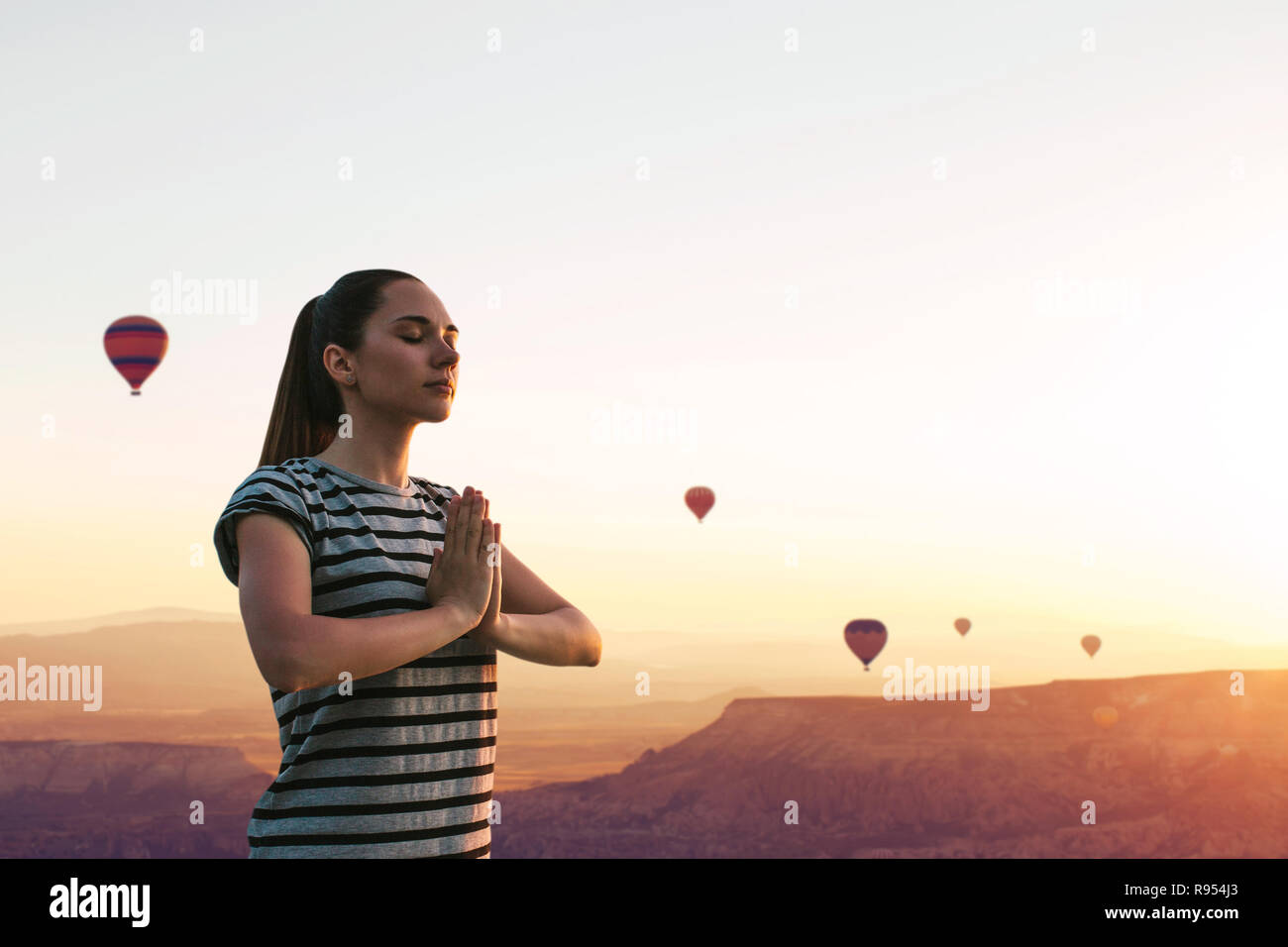 Ein Mädchen übt Yoga oder Meditation oder der Suche nach einer Seele vor dem Hintergrund der einen wunderschönen Sonnenuntergang und Luftballons in Kappadokien in der Türkei. Einsamkeit und unplugged Stockfoto