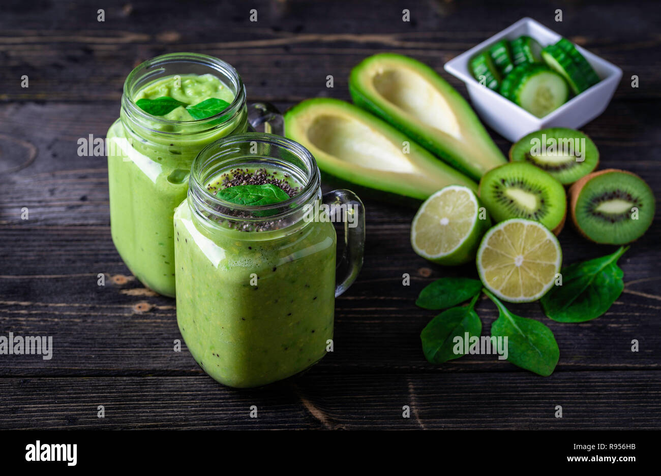 Grüne Smoothie auf dunklem Hintergrund mit Avocado, Spinat, Zitrone und Kiwi auf der rechten Seite. Stockfoto