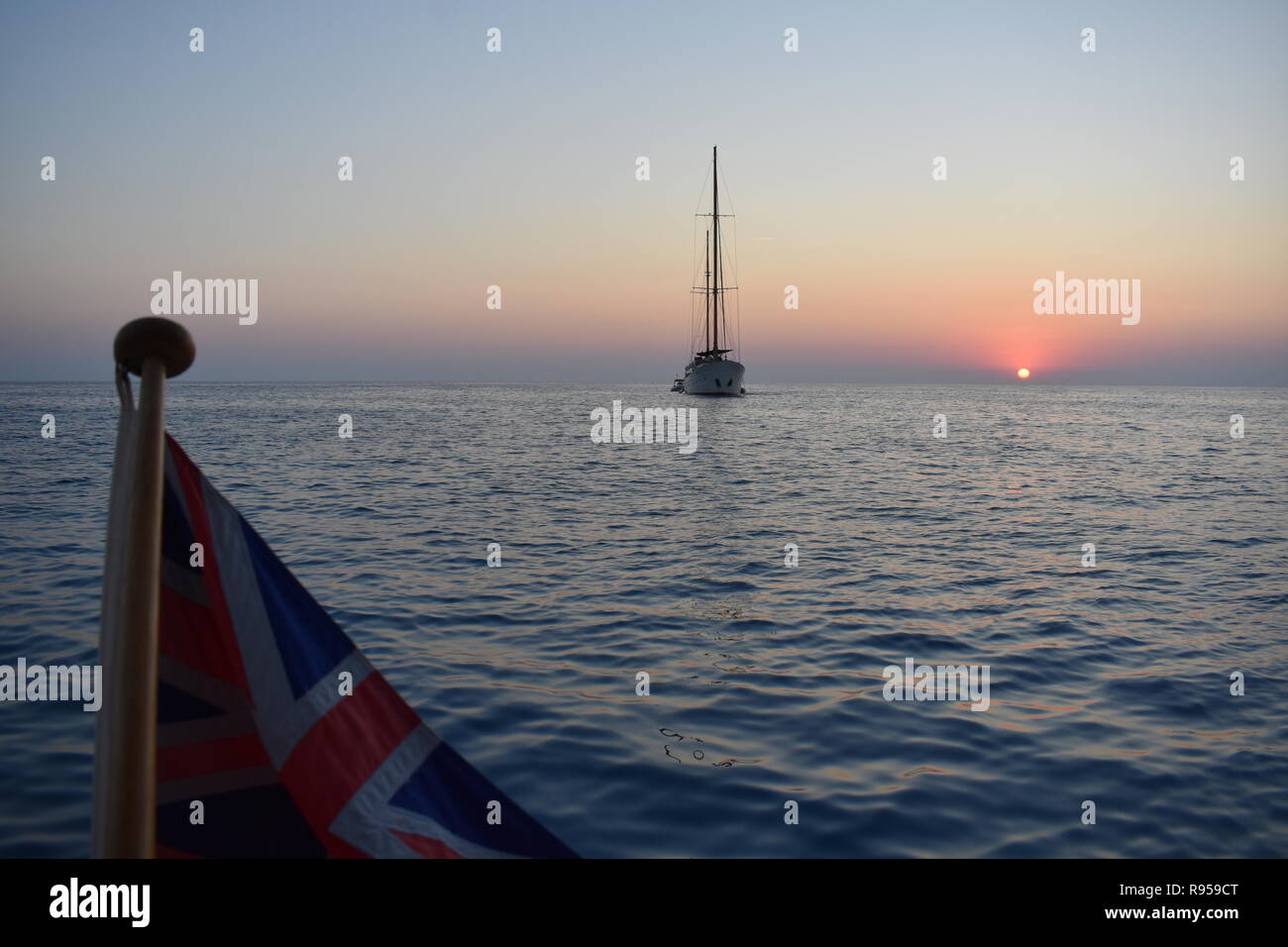 Blick auf einer Yacht und den Sonnenuntergang mit einem Britischen Fähnrich im Vordergrund, Cala Saona, Formentera, Spanien Stockfoto