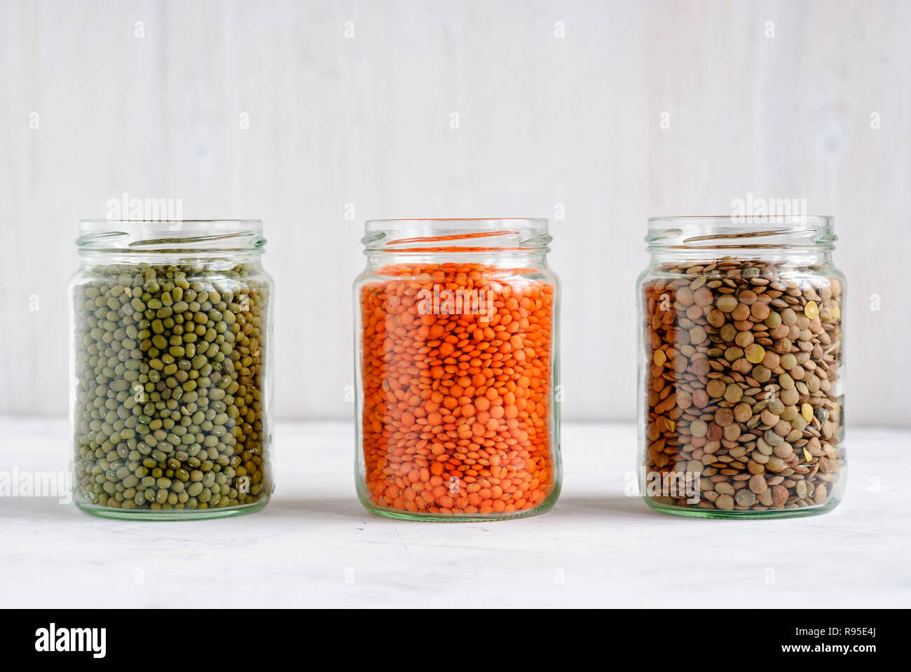 Getrocknete Mung Bohnen, grüne und rote Linsen aus Glas Vorratsgefäße in einer Reihe stehen auf weißen für gesunde vegetarische und vegane Küche Stockfoto