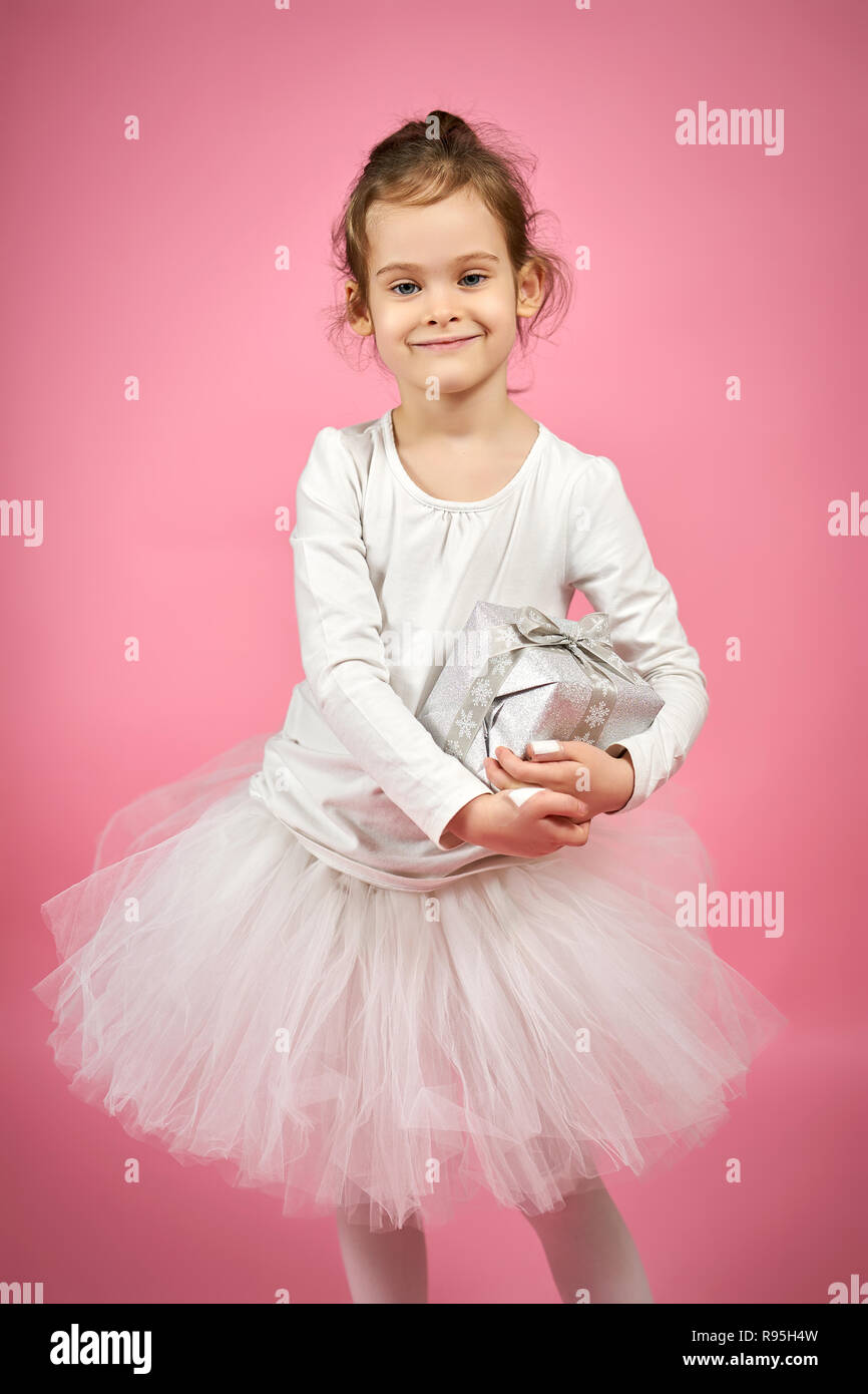 Süße kleine Mädchen in weißen Tüll Rock hält ein Geschenk auf einem rosa Hintergrund Stockfoto