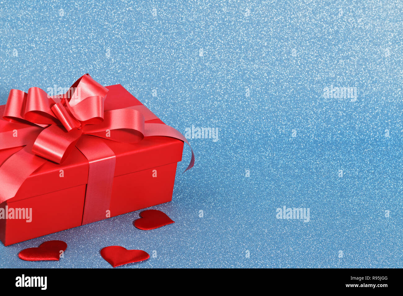 Nahaufnahme von einem roten Kästchen mit einem Geschenk und Herzen auf einem blauen glänzenden Hintergrund mit kopieren. Valentine's Day Feier Konzept. Stockfoto