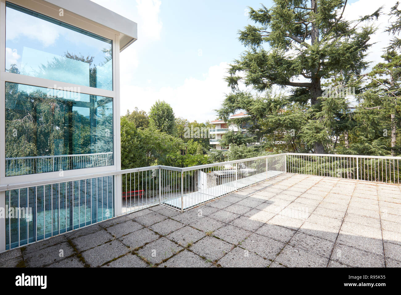 Große Terrasse im Landhaus mit großen Bäumen und Aufzug aus Glas Stockfoto