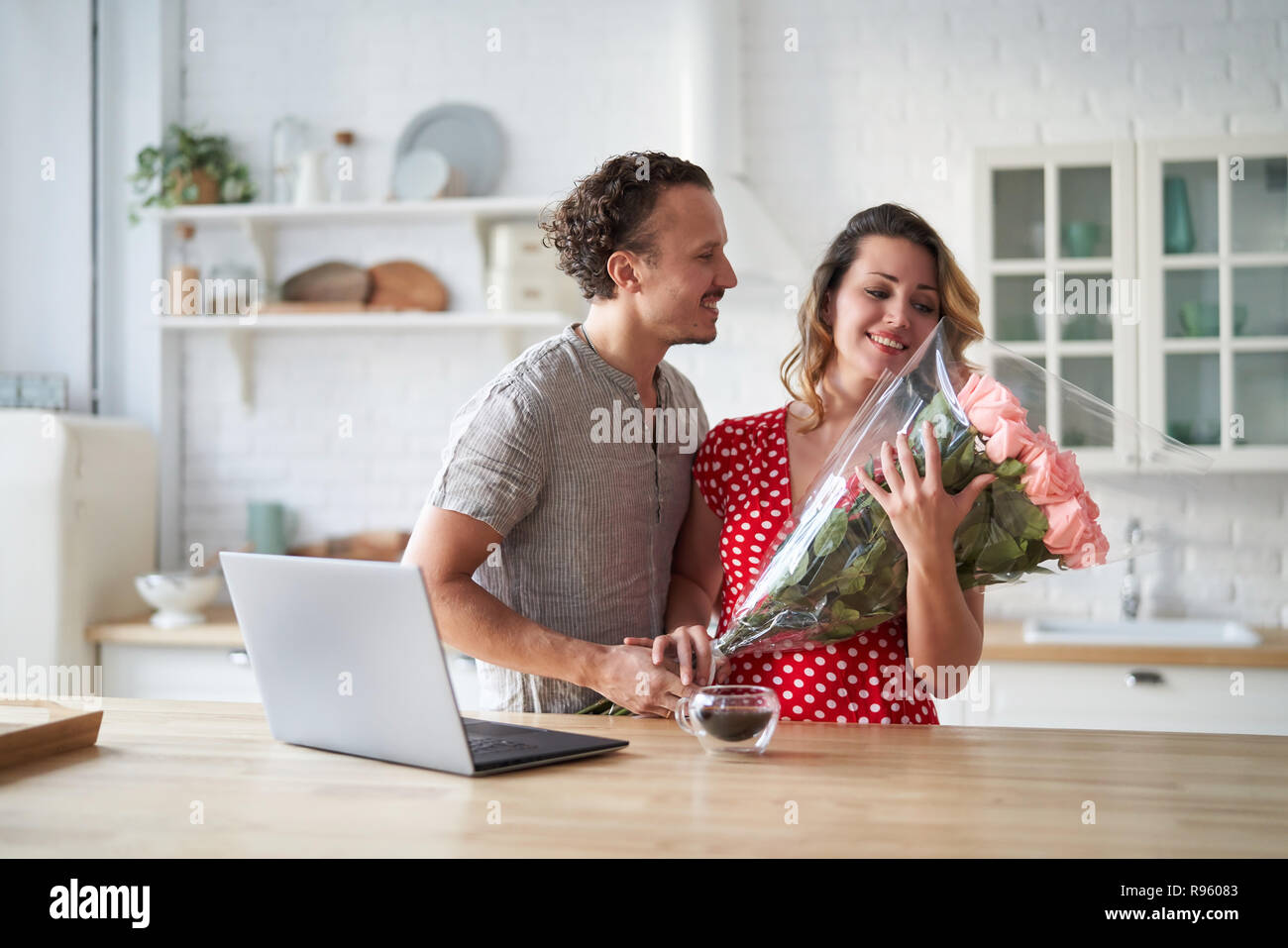 Lassen Sie sich überraschen. Wunderschönes romantisches Paar in der Küche. Junge präsentiert man Blumen zu seinen Geliebten. Das Gefühl von Glück. Stockfoto
