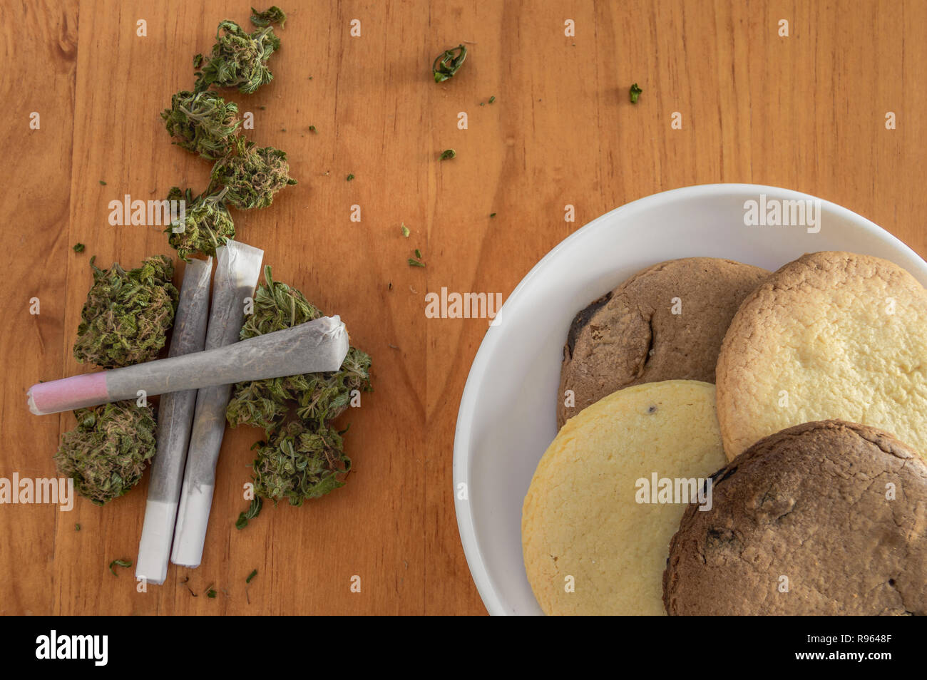 Stapel von Marihuana Knospen mit gewalzten Gelenke und einen Teller mit hausgemachten Keksen von Marihuana auf Holztisch. Frühstück von Unkraut und Cookies. Stockfoto