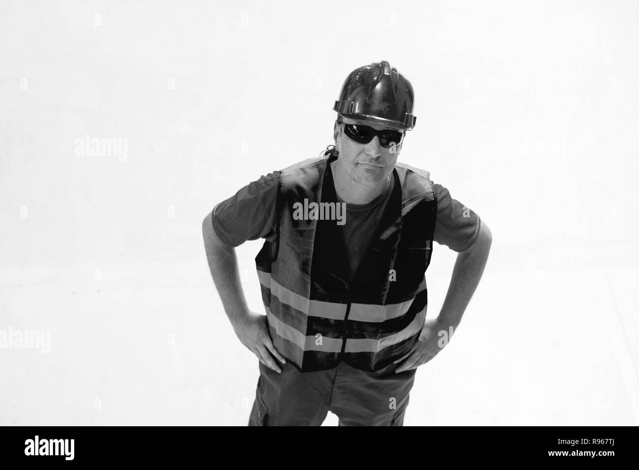 Schwarz-weiß Bild von Arbeiter, der sich mit den Armen auf seinen Hüften auf weißem Hintergrund. Stockfoto