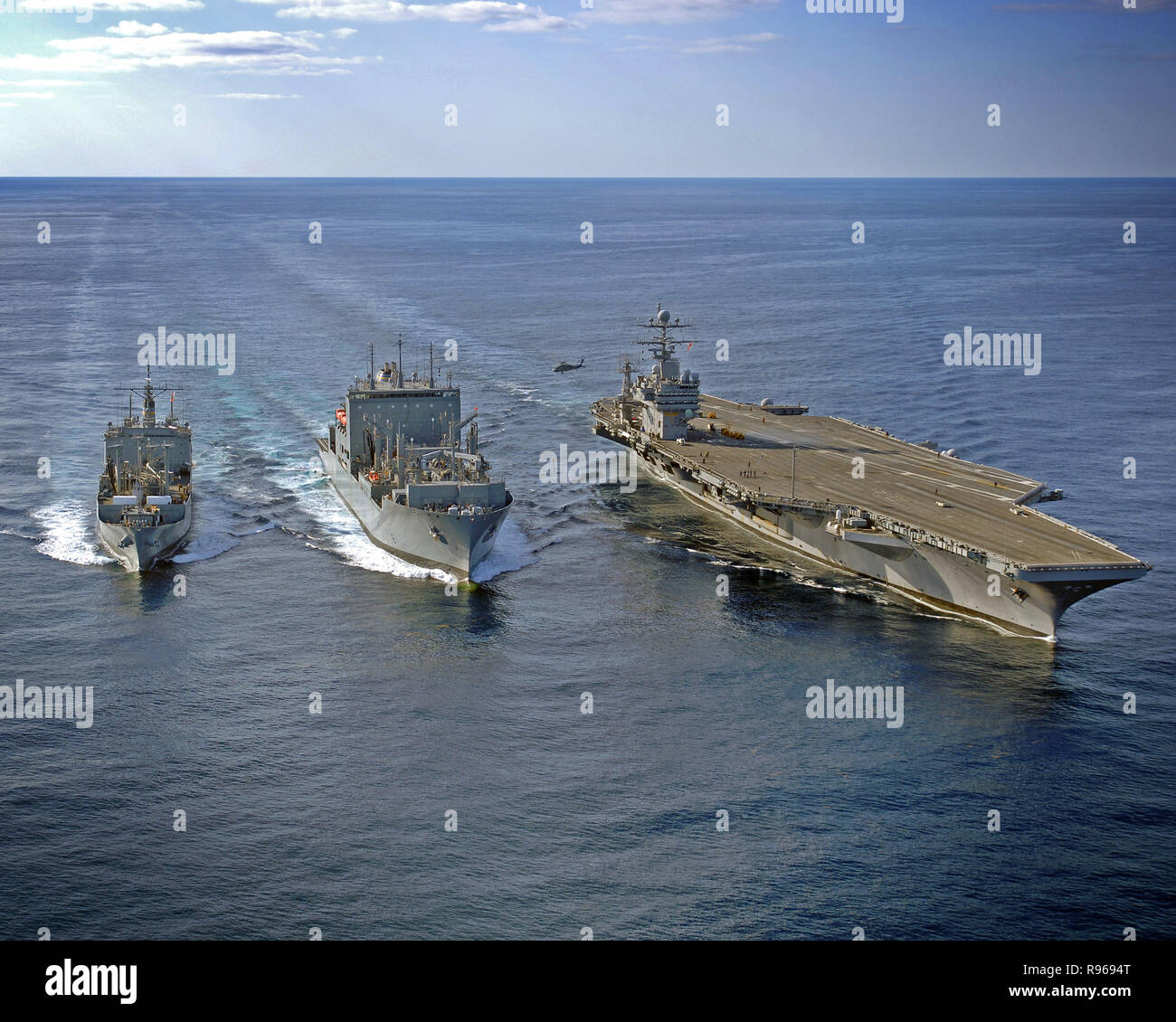 Ein MH-60 Seahawk Hubschrauber führt eine vertikale Nachschub mit Military Sealift Command Munition Schiff USNS Mount Baker (T-AE-34) und der USS Theodore Roosevelt (CVN-71). Foto: U.S. Navy Masse Kommunikation Spezialist Seemann Zach Hernandez Stockfoto