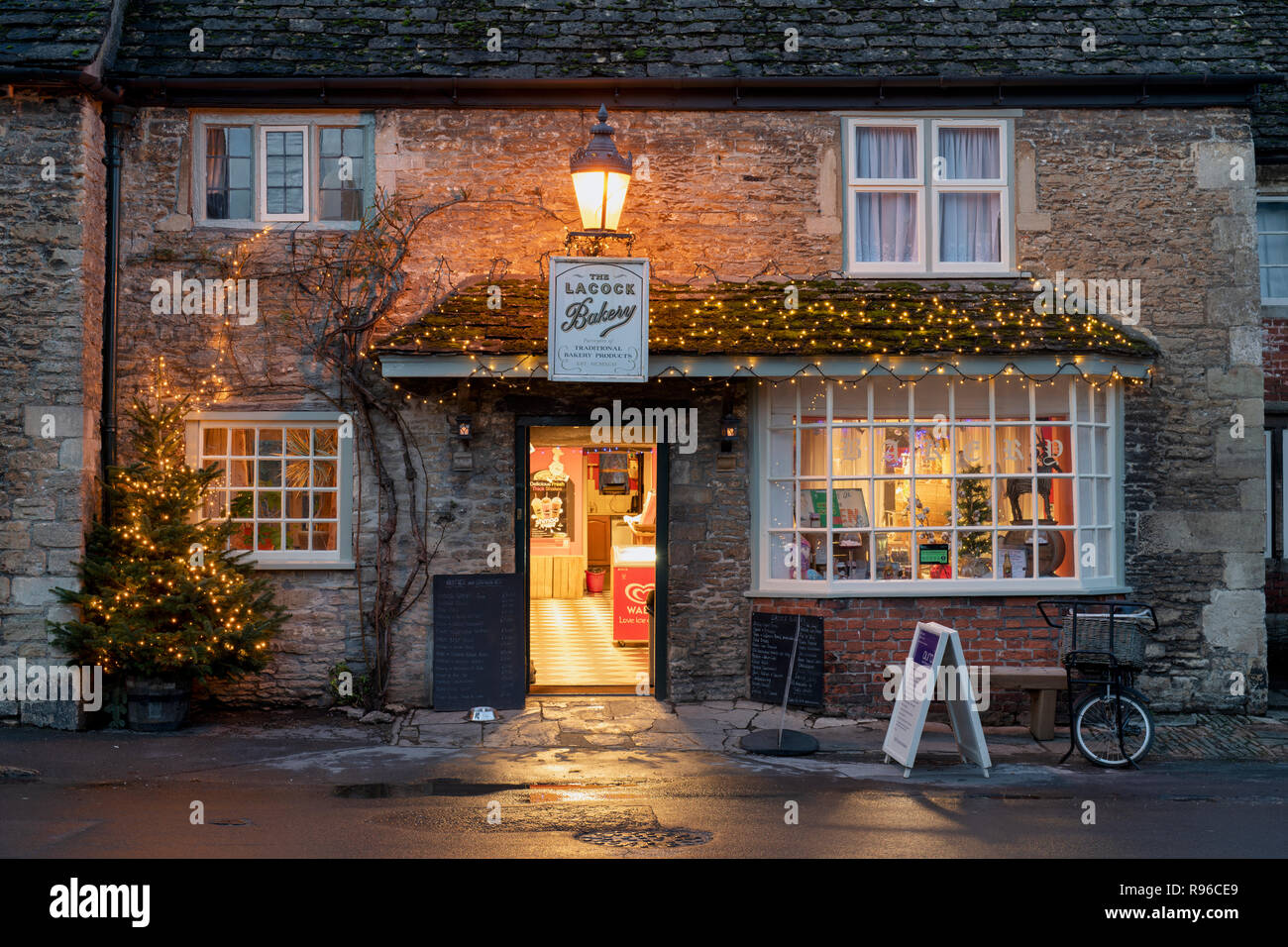 Lacock Dorf Bäckerei in der Nacht mit einem Weihnachtsbaum und Dekorationen. Lacock, Cotswolds, Wiltshire, England Stockfoto