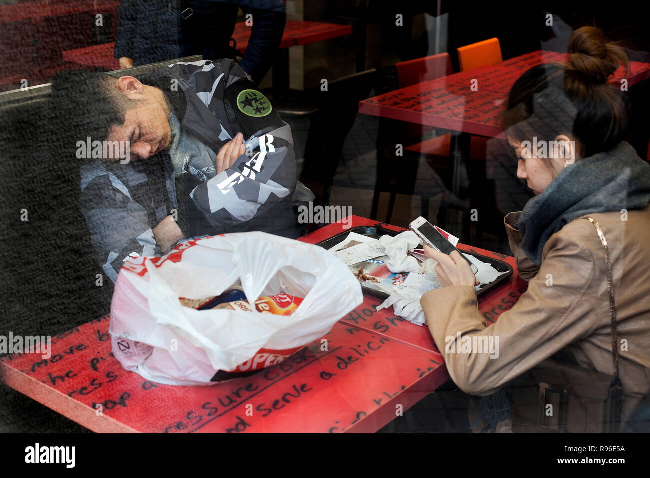 Asiatischer Mann schlafend in KFC während sein Partner ihr Smartphone verwendet, Barcelona, 2018. Stockfoto