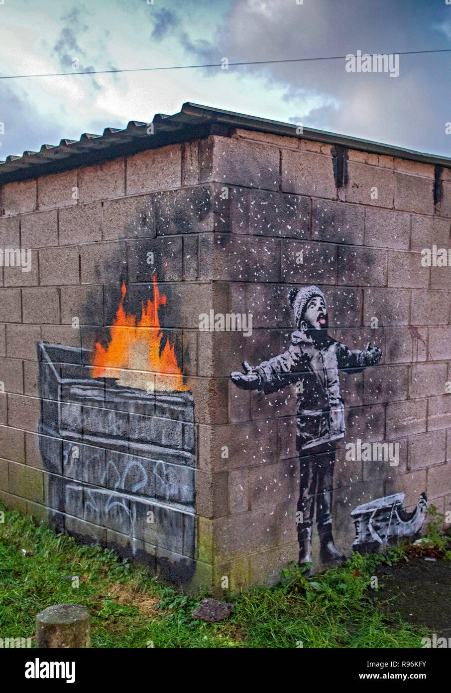 Port Talbot, Wales, UK. 19. Dezember, 2018. Neue graffiti in Port Talbot durch den anonymen Street Artist Banksy. Das Kunstwerk zeigt ein Kind mit offenen Armen spielen in, was scheint, Schnee mit dem Schlitten an seiner Seite zu sein, aber die andere Seite der Mauer zeigt, ist die Asche aus einem Mülleimer in Brand. Credit: Phil Rees/Alamy leben Nachrichten Stockfoto