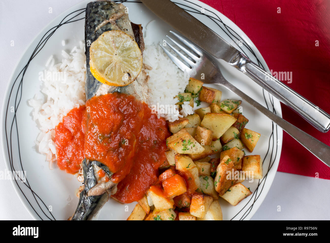 Ofen gebackene Makrelen auf einem Bett aus Reis mit sautierten Kartoffeln und eine Basilikum und Tomatensauce. Stockfoto