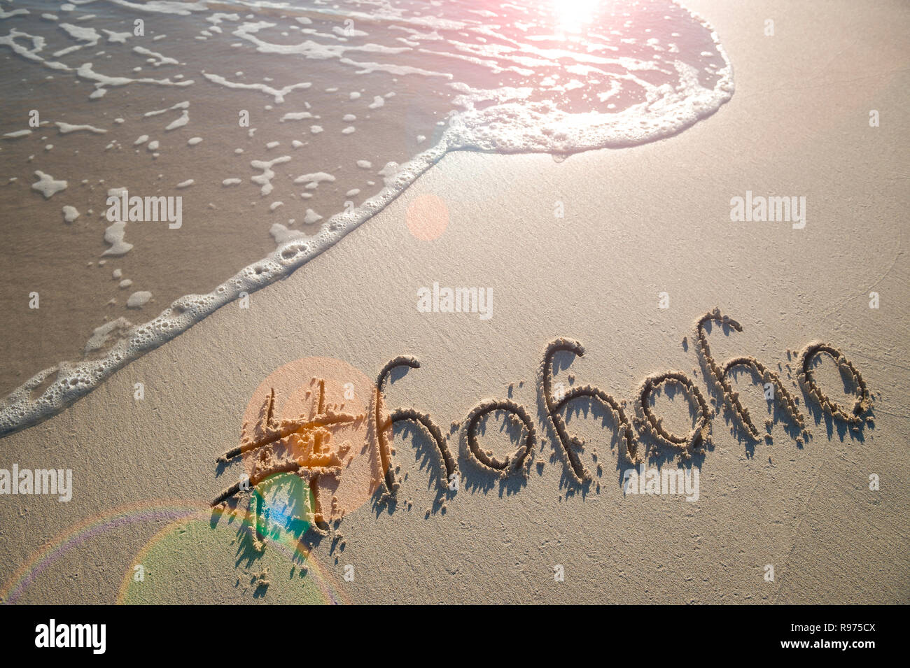 Moderne Ho-Ho-Ho Weihnachten Nachricht mit einem Hashtag für Social Media Sharing handschriftlich auf glatten Sand mit einem warmen tropischen Welle am Strand Stockfoto