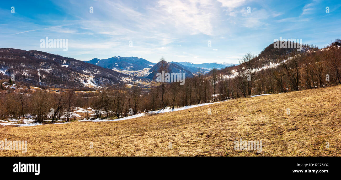 Panorama der bergigen Landschaft im Frühling. blattlosen Bäume und verwitterten Gras auf einer Wiese. Flecken Schnee auf die bewaldeten Hügel. wunderschöne blaue Stockfoto