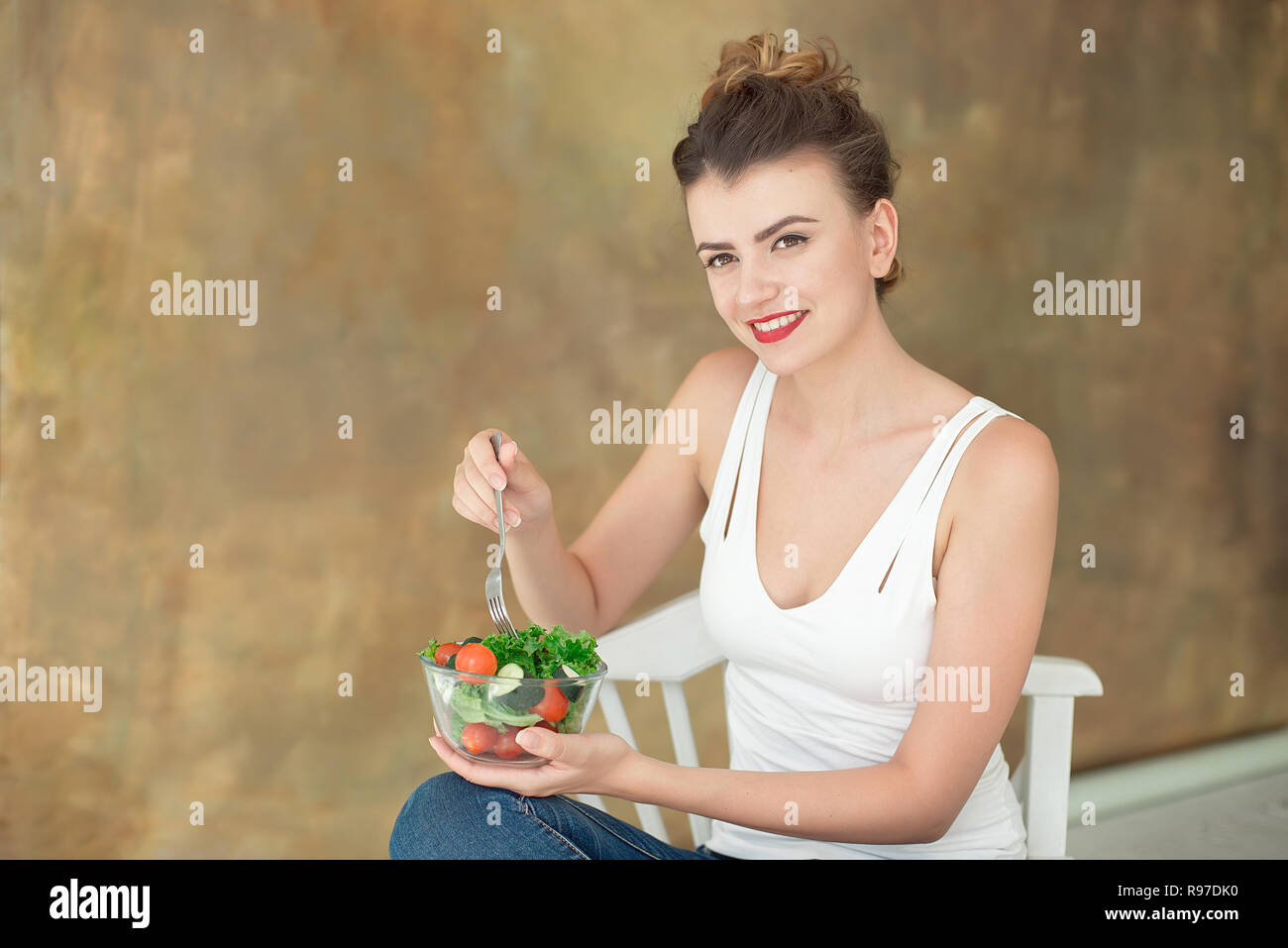 Wunderschöne gesunde Frau auf einem weißen Stuhl Essen einer gesunden Salat aus Rucola, Bio Tomaten Stockfoto