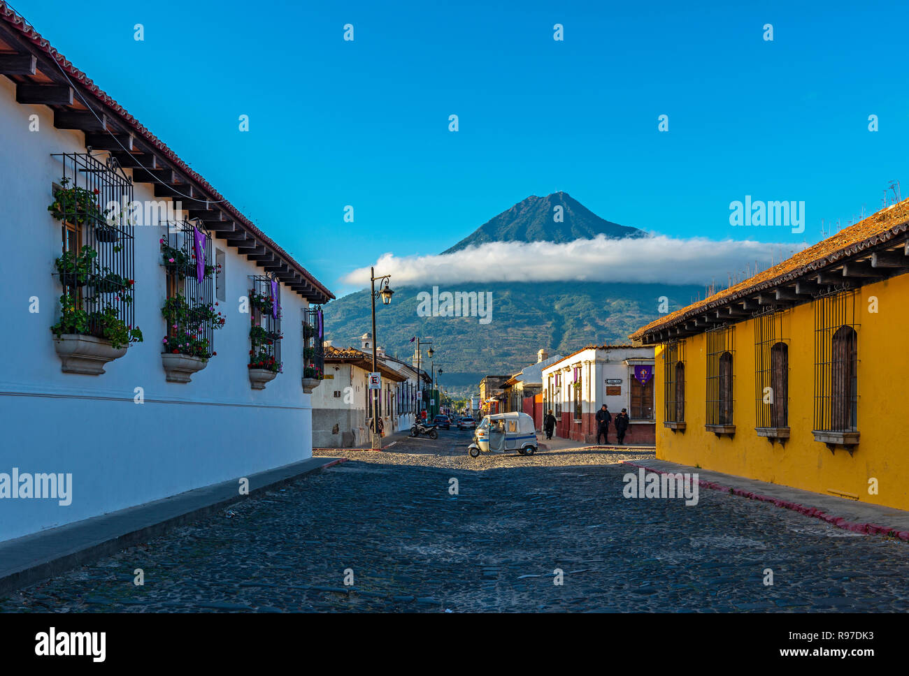 Ein mototaxi vorbei an einer Kreuzung bei Sonnenaufgang im historischen Zentrum von Antigua mit dem Agua Vulkan im Hintergrund, Guatemala. Stockfoto