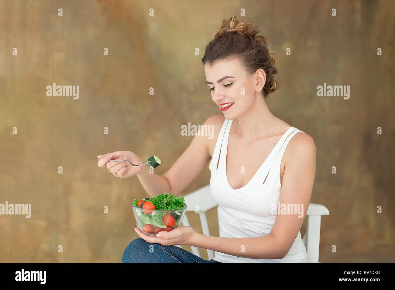 Wunderschöne gesunde Frau auf einem weißen Stuhl Essen einer gesunden Salat aus Rucola, Bio Tomaten Stockfoto