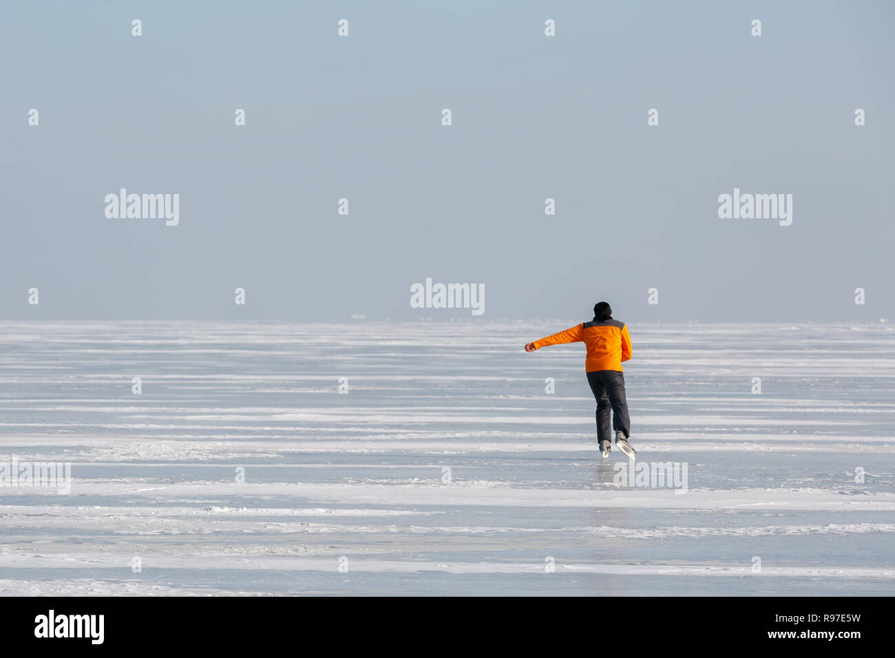 Junge Mann in einem orange Sweatshirt allein Schlittschuhen auf dem Eis eines zugefrorenen Meer Bay Stockfoto
