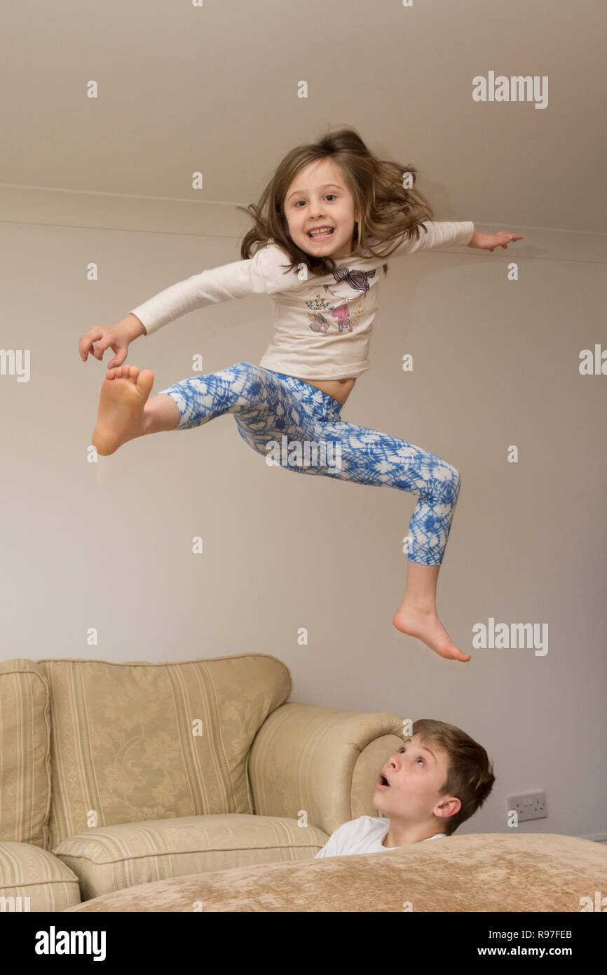 Kinder, Bruder und Schwester springen über auf Möbel, Tauchen und Springen, hyperaktiv, viel Energie, die zusammen spielen Stockfoto